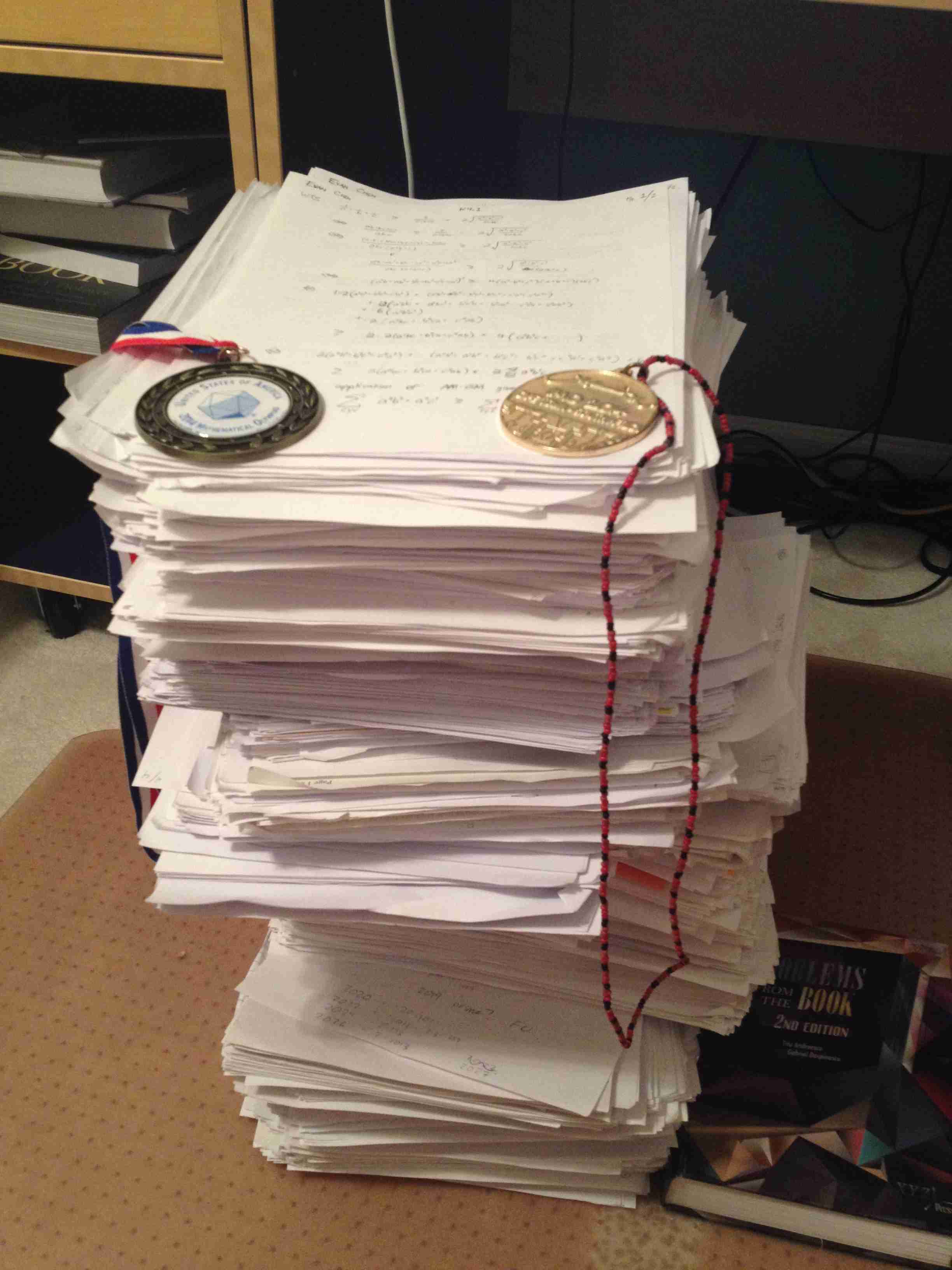 A stack of scratch paper from Evan's math contest career, with a USAMO winner medal and an IMO gold medal on top.